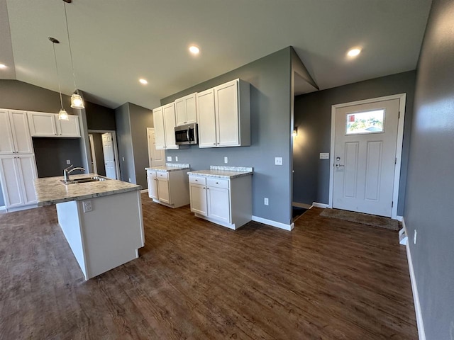 kitchen featuring white cabinetry, dark hardwood / wood-style flooring, lofted ceiling, decorative light fixtures, and a center island with sink