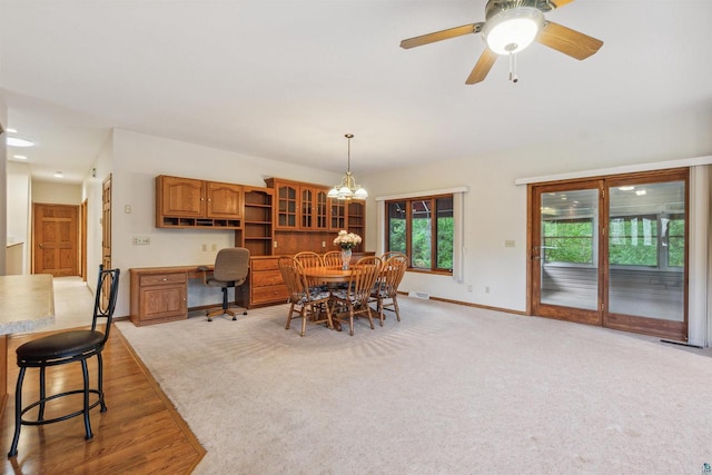 dining room with light carpet, ceiling fan with notable chandelier, and built in desk