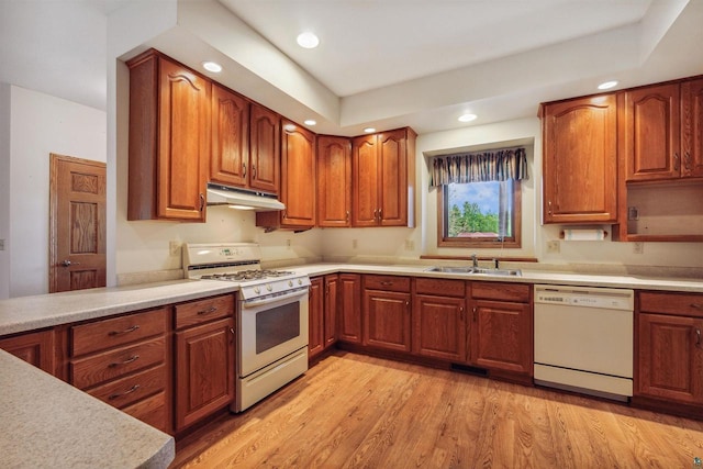 kitchen with light wood-type flooring, a raised ceiling, white appliances, and sink