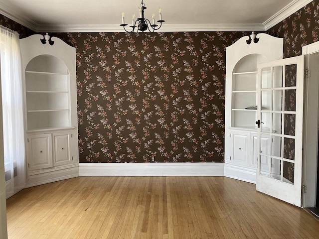 empty room featuring wood-type flooring, crown molding, a chandelier, and built in shelves