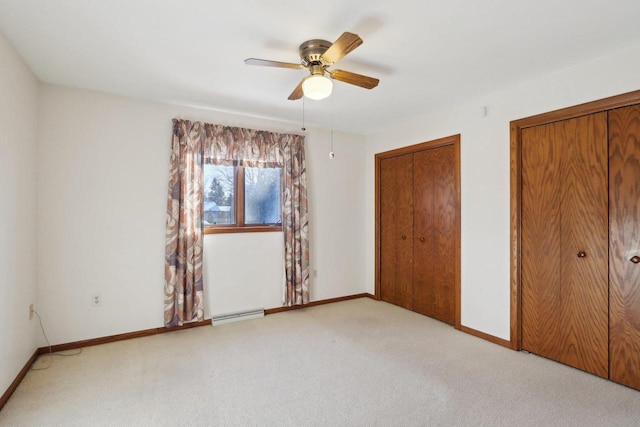 unfurnished bedroom featuring multiple closets, light colored carpet, ceiling fan, and baseboard heating