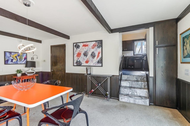 dining room featuring beam ceiling, wood walls, an inviting chandelier, and light colored carpet