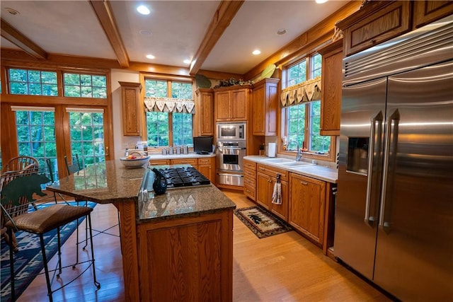 kitchen featuring a center island, built in appliances, sink, beam ceiling, and a healthy amount of sunlight