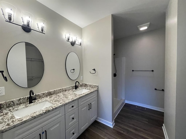 full bathroom featuring double vanity, baseboards, walk in shower, and a sink