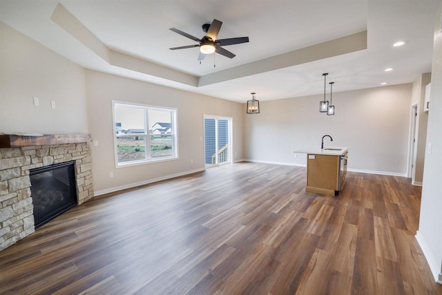 889 Red Hawk Dr, Milton, WI 53563 - unfurnished living room featuring a stone fireplace, dark wood-style floors, a ceiling fan, a raised ceiling, and recessed lighting