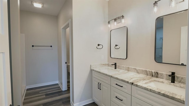 full bath with double vanity, wood finished floors, baseboards, and a sink