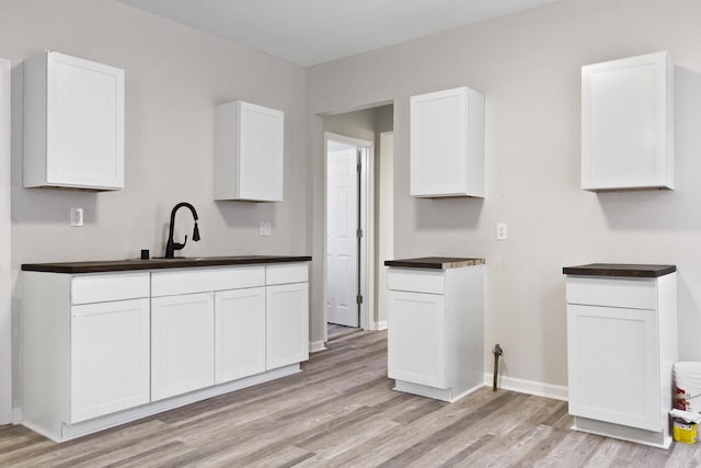 kitchen with light wood-type flooring, white cabinetry, and sink