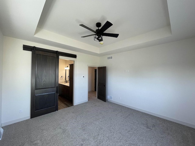 unfurnished bedroom featuring a barn door, a tray ceiling, connected bathroom, and ceiling fan