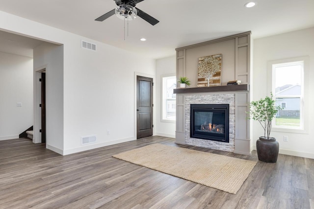 unfurnished living room featuring a healthy amount of sunlight, ceiling fan, a fireplace, and wood-type flooring