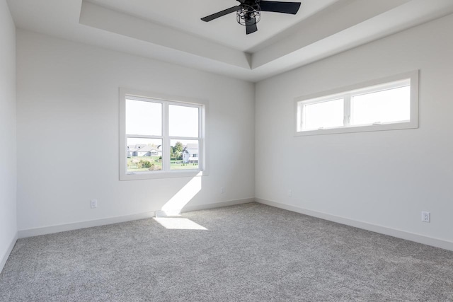 carpeted empty room featuring ceiling fan, a wealth of natural light, and a raised ceiling