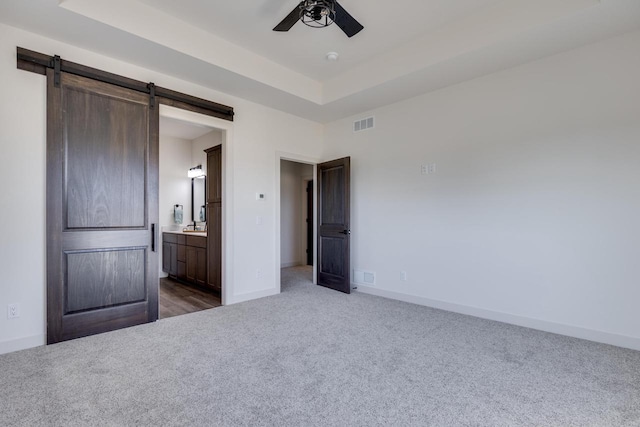 unfurnished bedroom with a barn door, dark carpet, connected bathroom, and ceiling fan