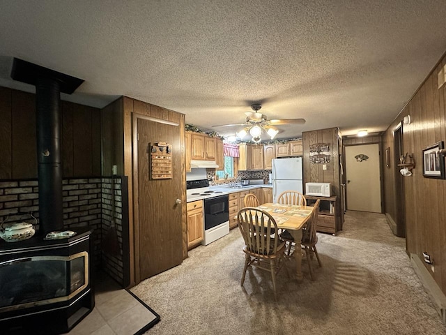 kitchen featuring a wood stove, wood walls, light colored carpet, white appliances, and ceiling fan