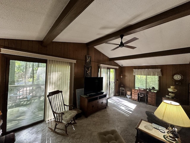 living room featuring wood walls, carpet flooring, lofted ceiling with beams, and ceiling fan