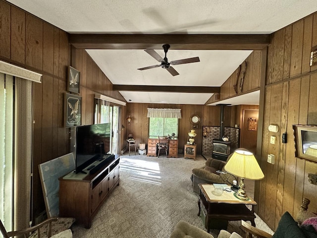 living room featuring lofted ceiling with beams, carpet flooring, a wood stove, wood walls, and ceiling fan