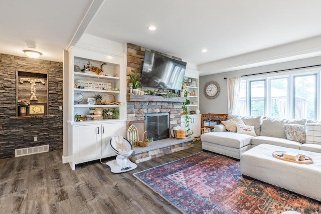 living room with built in features, dark wood-type flooring, and a stone fireplace