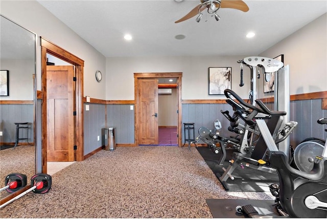 exercise room featuring carpet, wood walls, and ceiling fan