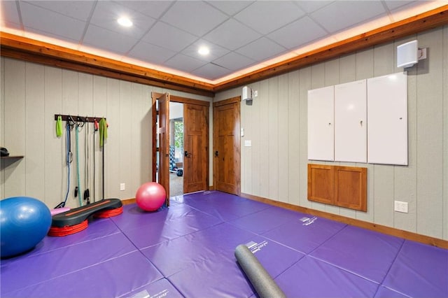 workout room featuring wooden walls, a drop ceiling, and tile patterned floors