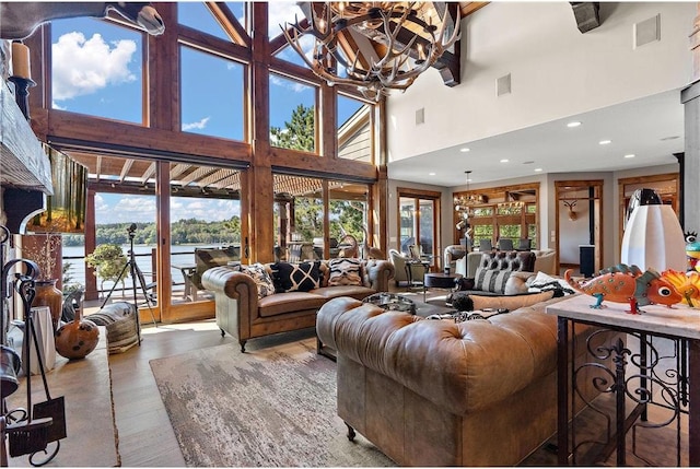 living room with an inviting chandelier, hardwood / wood-style floors, a water view, and a towering ceiling