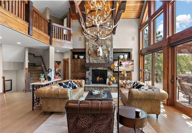 living room featuring wood ceiling, light hardwood / wood-style floors, a notable chandelier, high vaulted ceiling, and a stone fireplace