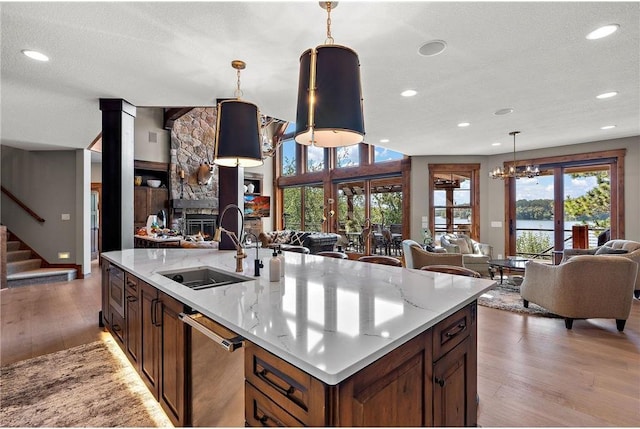 kitchen with light hardwood / wood-style floors, a textured ceiling, a kitchen island with sink, hanging light fixtures, and a fireplace