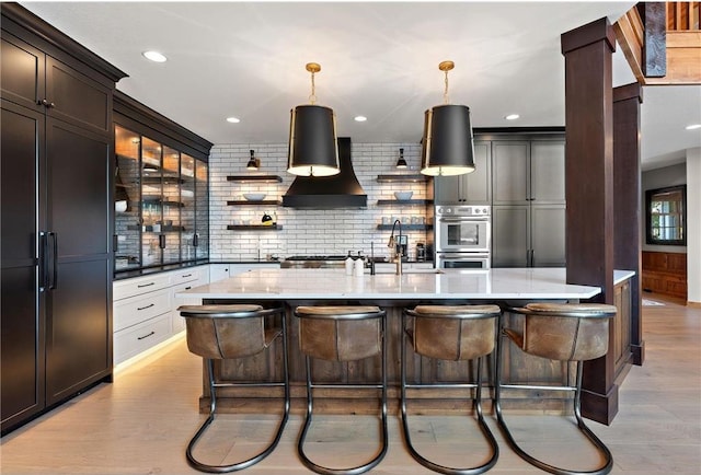 kitchen with white cabinets, light hardwood / wood-style flooring, wall chimney range hood, a kitchen breakfast bar, and stainless steel appliances