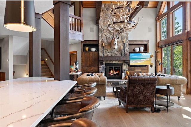 living room featuring a chandelier, beamed ceiling, a fireplace, high vaulted ceiling, and light hardwood / wood-style flooring