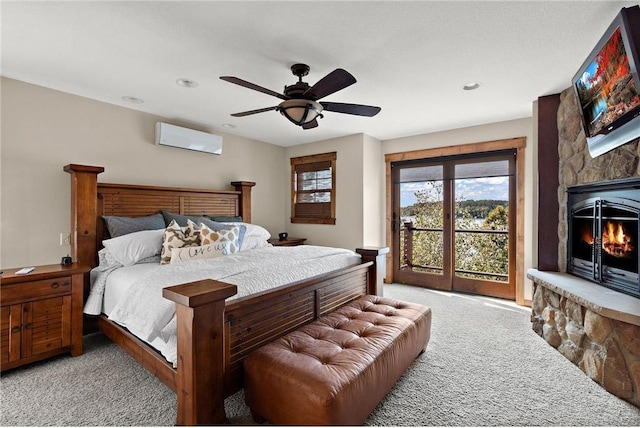 carpeted bedroom featuring access to outside, a fireplace, a wall mounted air conditioner, and ceiling fan