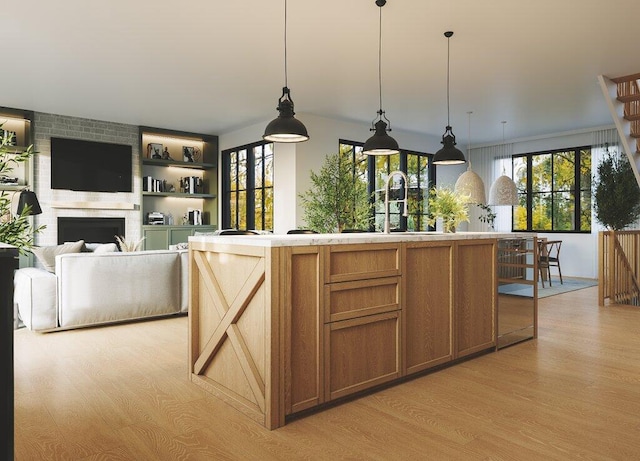 kitchen with sink, light hardwood / wood-style floors, a fireplace, a large island, and decorative light fixtures