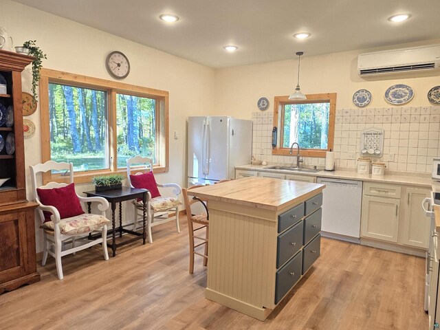 kitchen with pendant lighting, white cabinetry, a kitchen island, white appliances, and a wall mounted AC