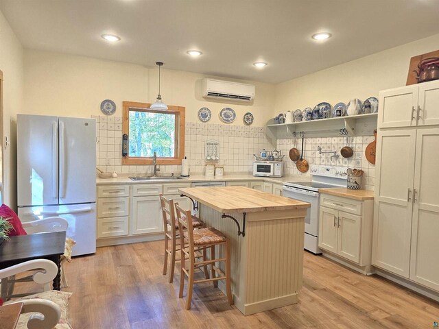 kitchen featuring hanging light fixtures, white appliances, butcher block counters, sink, and a wall mounted air conditioner