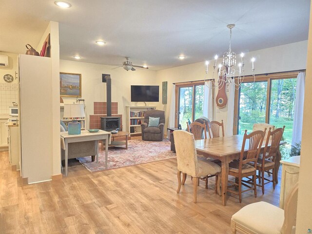 dining space with ceiling fan with notable chandelier, a wall mounted air conditioner, a wood stove, and light hardwood / wood-style flooring