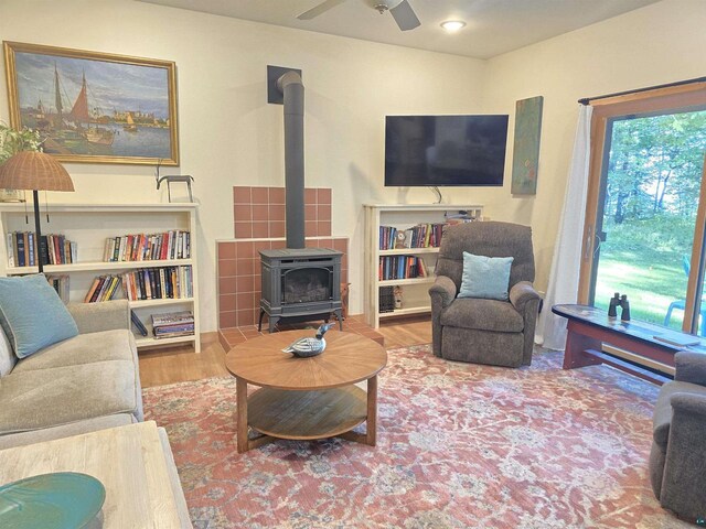 living room with a wood stove, ceiling fan, and wood-type flooring