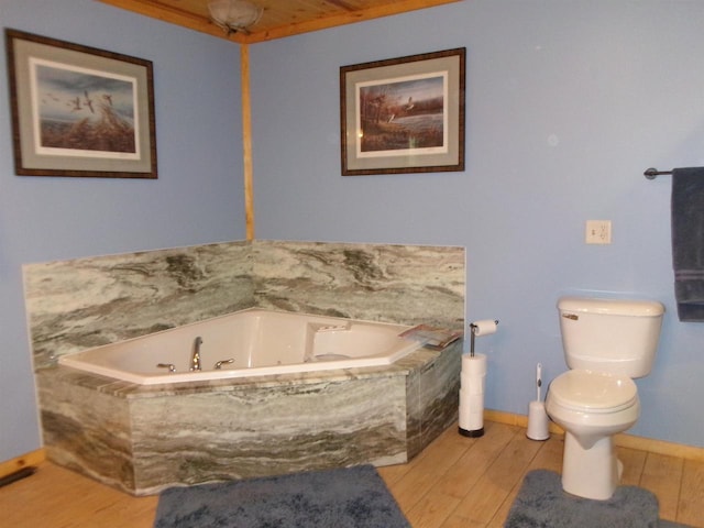 bathroom with hardwood / wood-style flooring, a relaxing tiled tub, and toilet