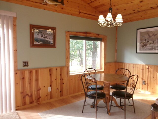 dining area with wood walls, light hardwood / wood-style flooring, wooden ceiling, a notable chandelier, and vaulted ceiling