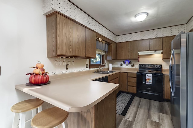 kitchen featuring kitchen peninsula, black / electric stove, sink, a kitchen breakfast bar, and stainless steel fridge