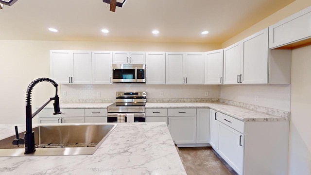 kitchen featuring appliances with stainless steel finishes, light stone counters, white cabinetry, a sink, and recessed lighting