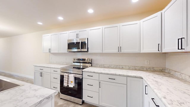 kitchen with light stone counters, tasteful backsplash, white cabinetry, appliances with stainless steel finishes, and light wood-type flooring