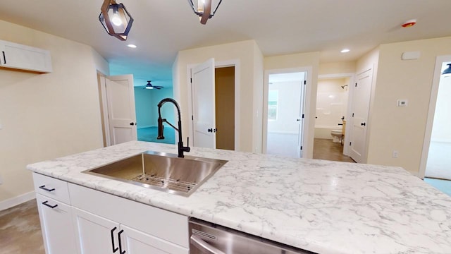 kitchen with light stone counters, dishwasher, sink, white cabinetry, and ceiling fan