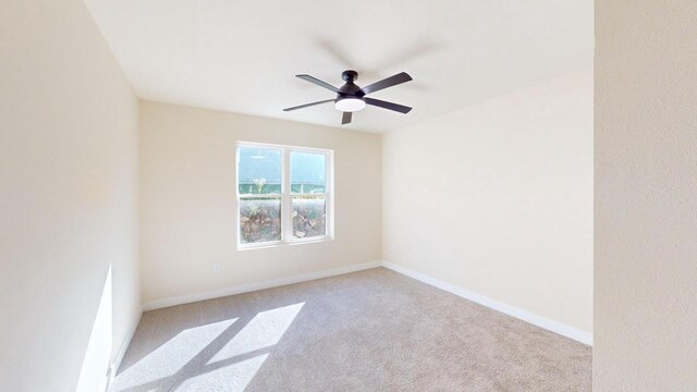 spare room featuring light colored carpet, ceiling fan, and baseboards