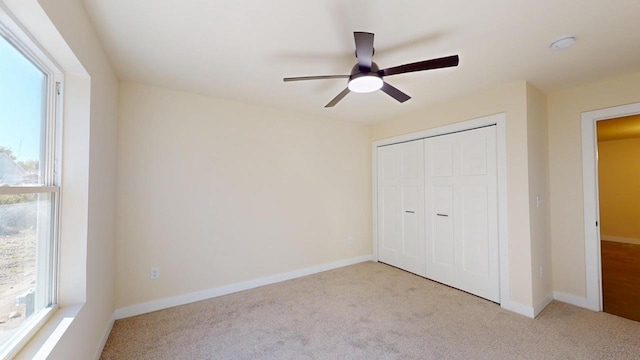 unfurnished bedroom with baseboards, ceiling fan, a closet, and light colored carpet