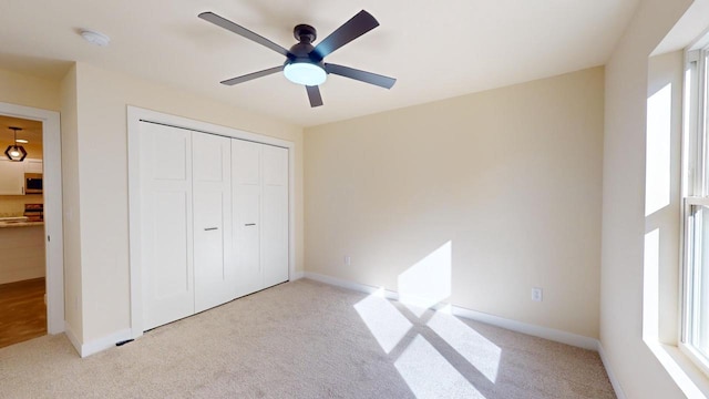 unfurnished bedroom featuring ceiling fan, baseboards, a closet, and light colored carpet