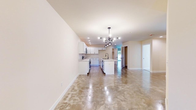 interior space featuring hanging light fixtures, sink, concrete floors, white cabinetry, and a center island