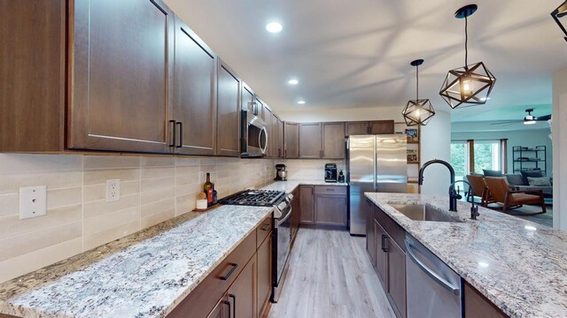 kitchen with appliances with stainless steel finishes, light stone countertops, ceiling fan, light hardwood / wood-style flooring, and sink