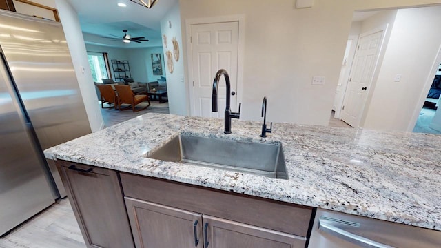 kitchen featuring vaulted ceiling, light stone counters, stainless steel appliances, ceiling fan, and sink