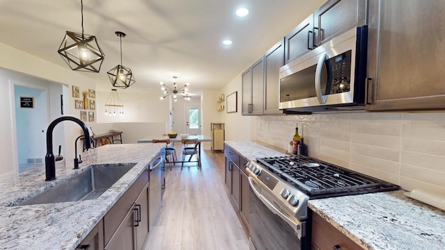 kitchen featuring light hardwood / wood-style floors, light stone countertops, pendant lighting, stainless steel appliances, and sink