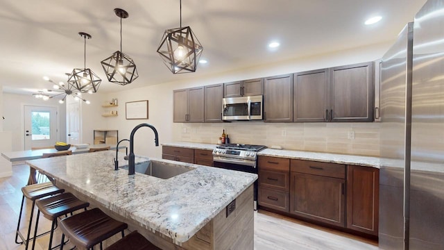 kitchen featuring hanging light fixtures, sink, a kitchen island with sink, stainless steel appliances, and light wood-type flooring