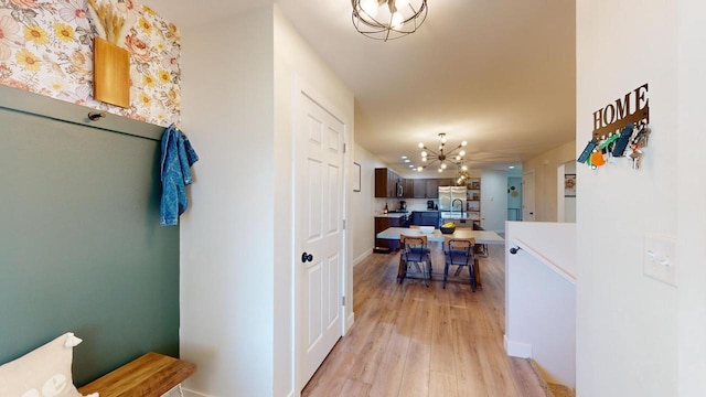 corridor with light wood-type flooring, sink, and a notable chandelier