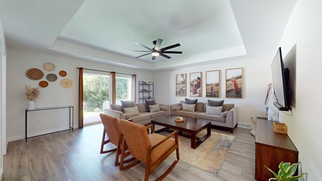 living room with light hardwood / wood-style flooring, a tray ceiling, and ceiling fan