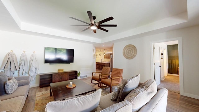 living room featuring ceiling fan, a tray ceiling, light wood-type flooring, and sink