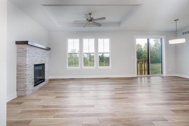 unfurnished living room featuring light hardwood / wood-style floors, ceiling fan, a tray ceiling, and a stone fireplace